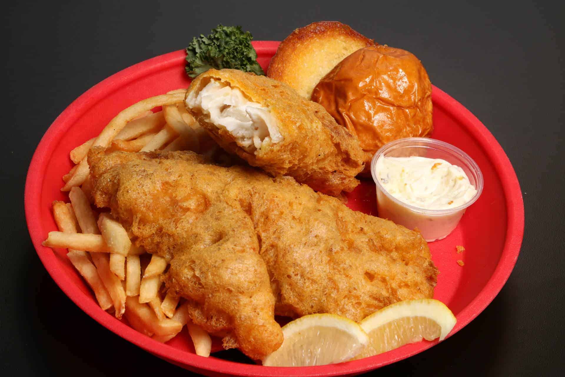 Fresh fried shrimp platter with sides at The Original Island Shrimp House. Fried shrimp with fries, bread roll, lemon wedges, and dipping sauce on a red plate.