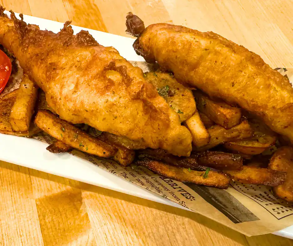 Shrimp Basket at The Original Island Shrimp House Tavern-style battered fish with fries on a platter, served with dipping sauce.